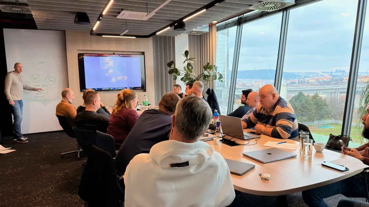 A presenter at a screen in a workshop room overlooking the Prague skyline