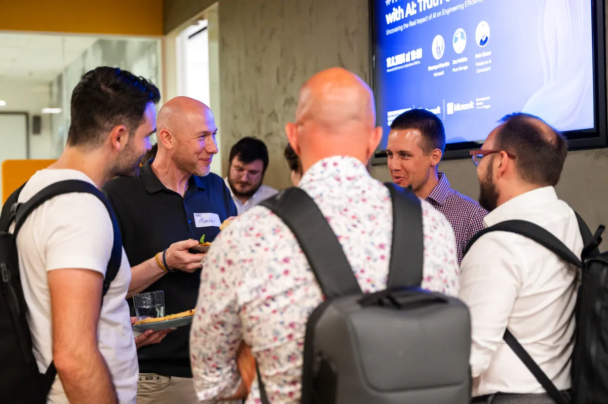 Engineering leaders holding drinks and plates talking together during the networking part of an ELC meetup, the event agenda on the screen behind them.