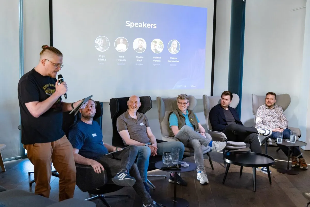 A moderator holding a microphone stands beside five seated panelists at an ELC meetup, in front of a slide titled Speakers.
