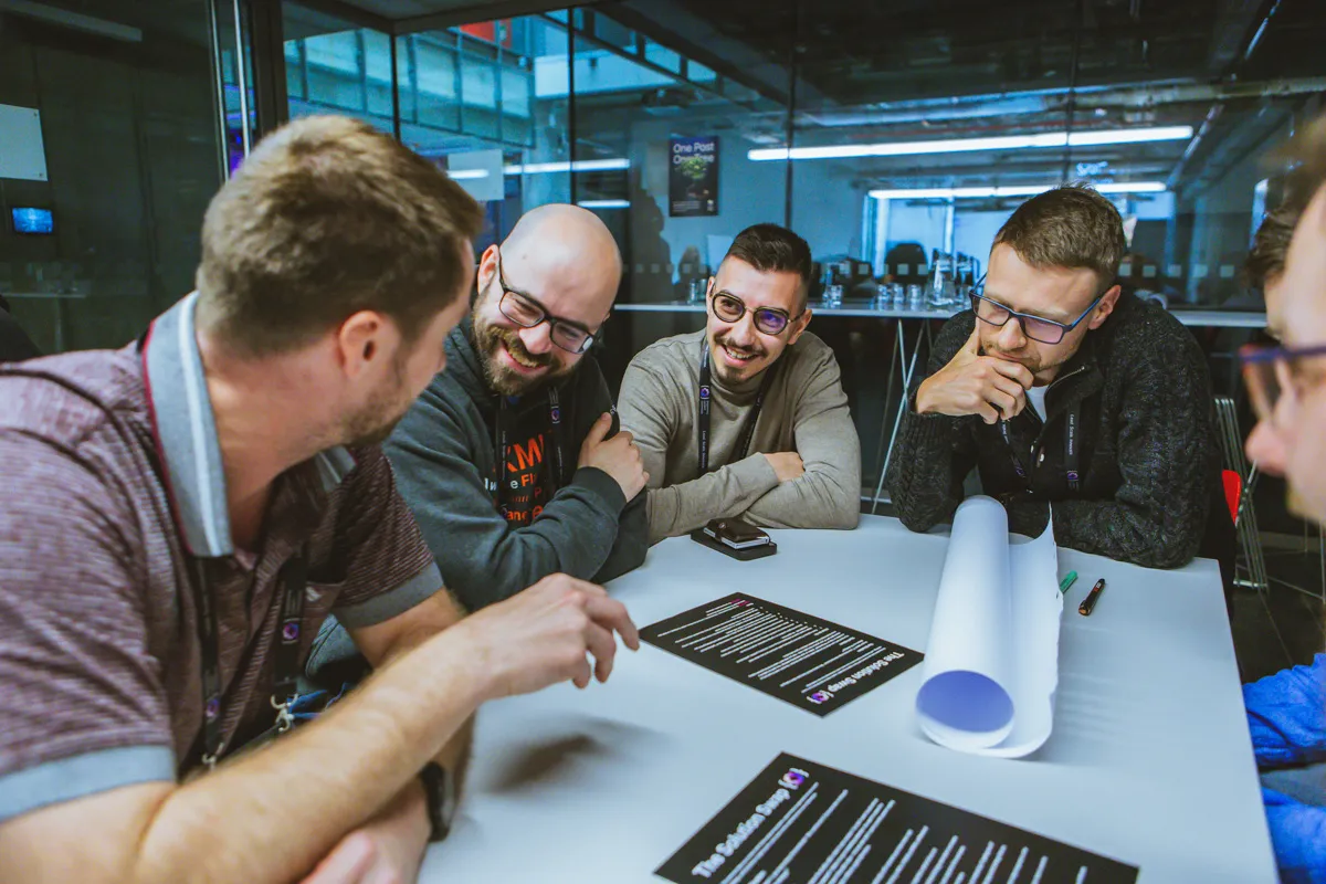 Five engineering leaders gathered around a table covered in printed worksheets, laughing during a workshop breakout at the ELC Conference.